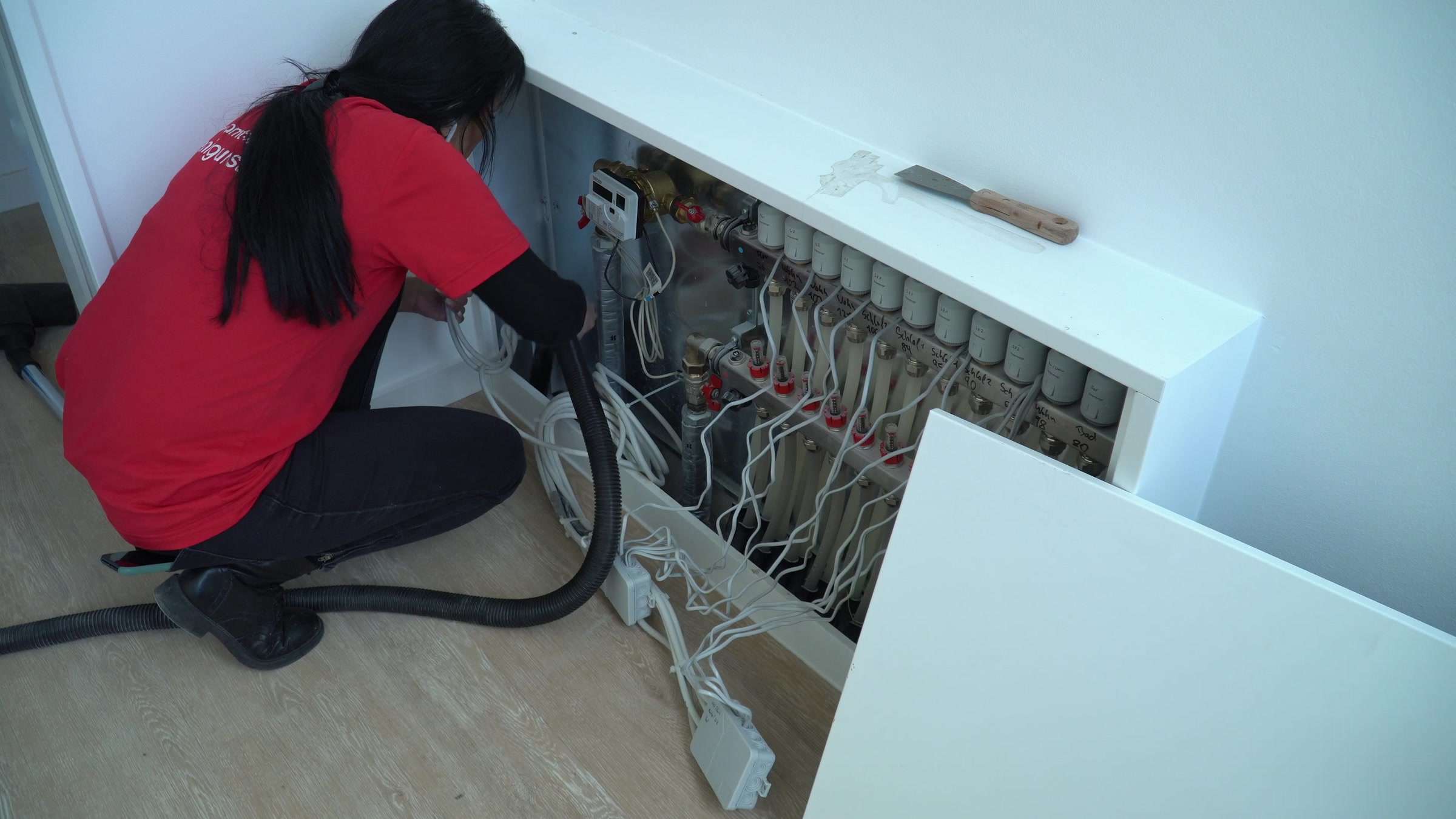 Bauendreinigung Berlin: Reinigungskraft der AMT multiservices saugt einen Heizkreisverteiler aus