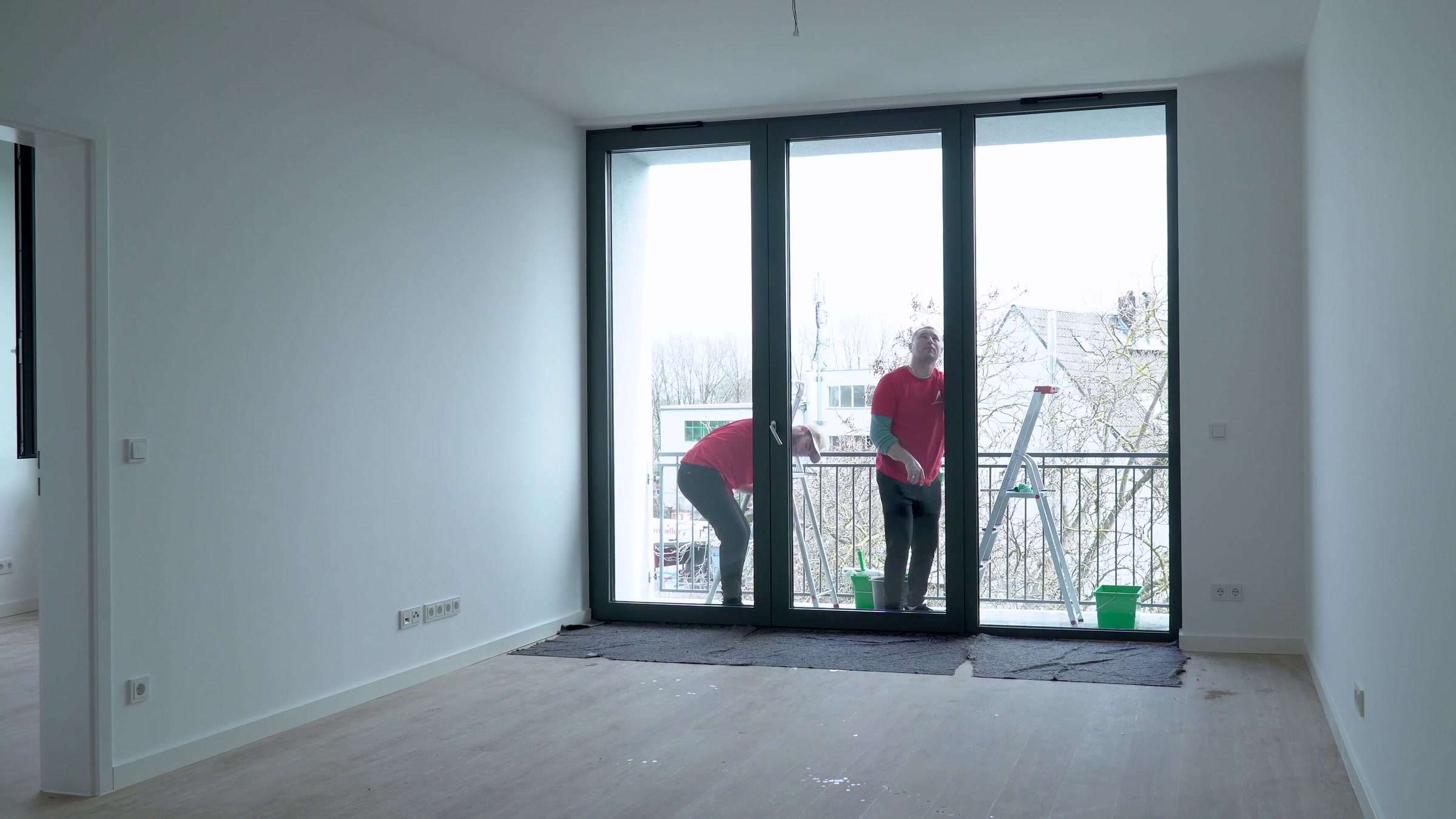 Gebäudereinigung Berlin: Zwei Reinigungskräfte der AMT multiservices reinigen die Balkontür einer Neubauwohnung