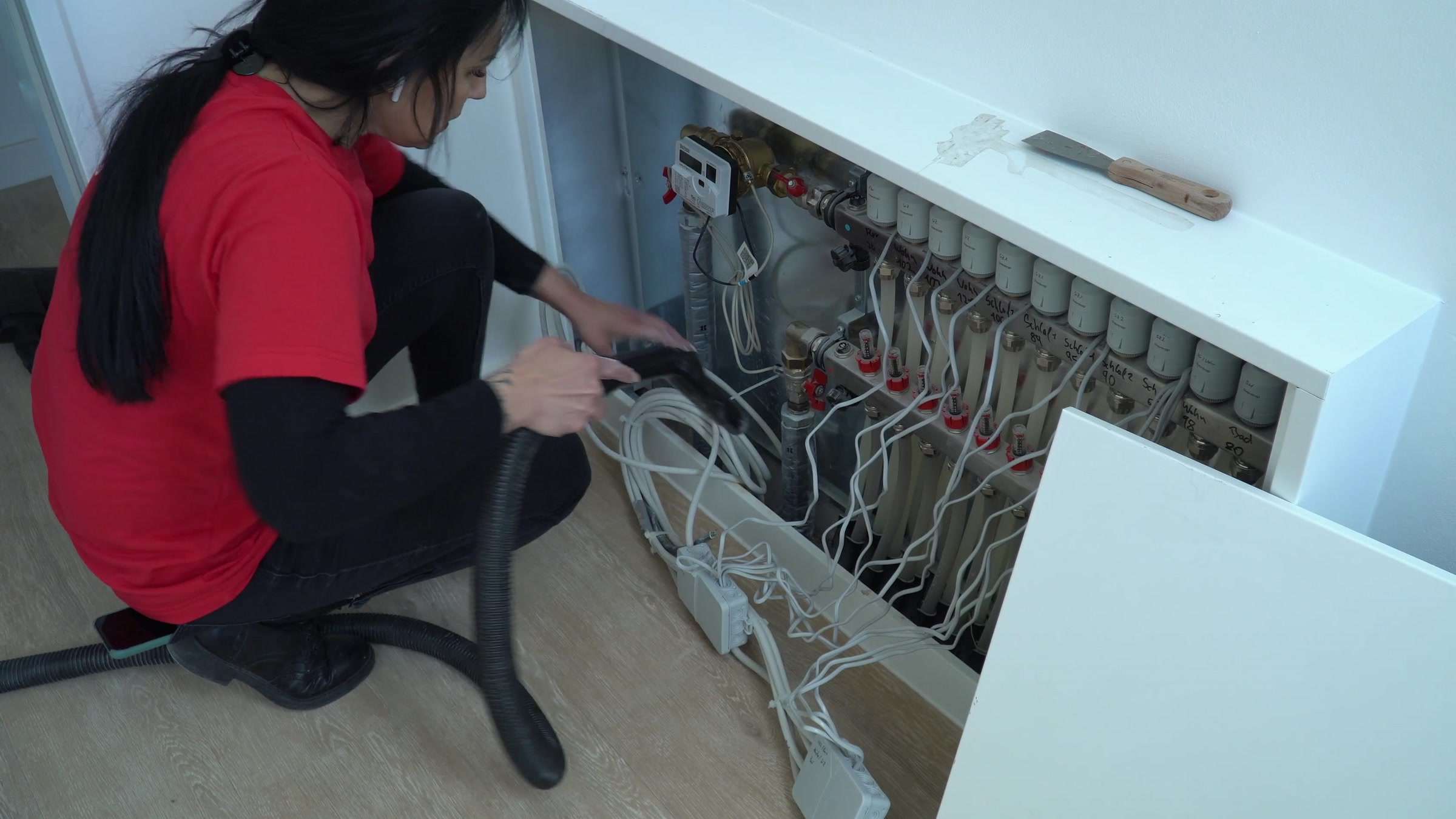 Bauendreinigung: Mitarbeiterin der AMT multiservices saugt den Heizkreisverteiler einer Neubauwohnung aus